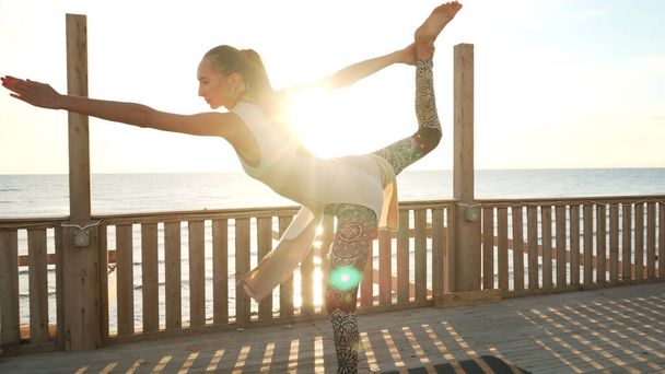 Flexible caucasian girl doing standing bow yoga pose on rooftop in sunshine. - Photo, Image