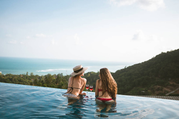 Beautiful girls having fun by the pool with wine and talking about travel and the weekend. Discuss March 8th. Holidays and parties by the pool in a villa by the sea. Thailand, Samui - Photo, image