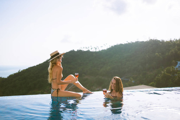 Beautiful girls having fun by the pool with wine and talking about travel and the weekend. Discuss March 8th. Holidays and parties by the pool in a villa by the sea. Thailand, Samui - Foto, Imagen