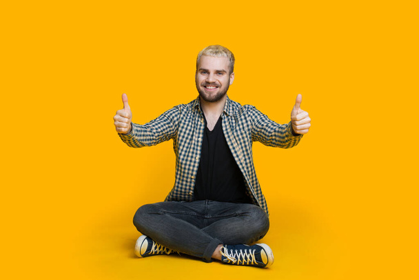 Bionda uomo caucasico con la barba è seduto su un muro giallo e gesticolare l'approvazione cantare
 - Foto, immagini