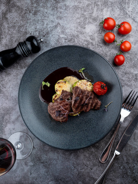Beef tenderloin medallions with mulled wine sauce with grilled vegetables on black plate - 写真・画像