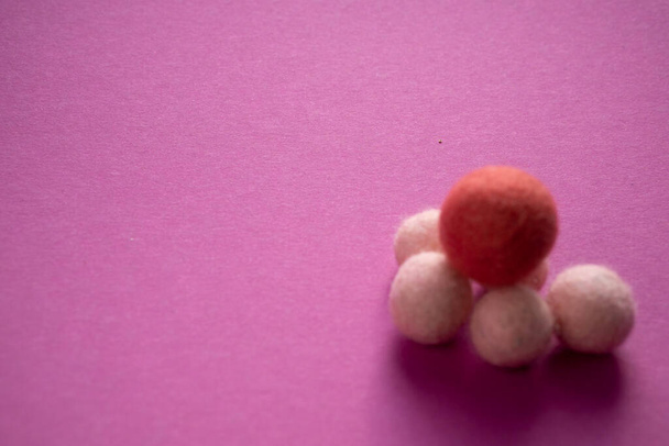 Groupe de grosses et petites boules de laine foncées et claires empilées sur une surface rose lisse. Feutrage à sec avec une aiguille
. - Photo, image