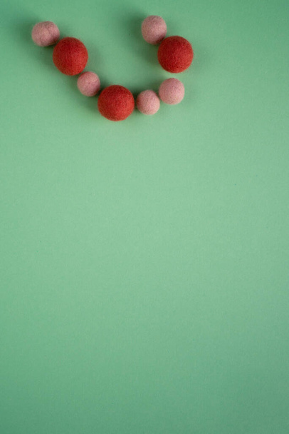 Великі темні і маленькі легкі вовняні кульки мають форму напівсерця на гладкій зеленій поверхні. Сухе фарбування голкою
. - Фото, зображення