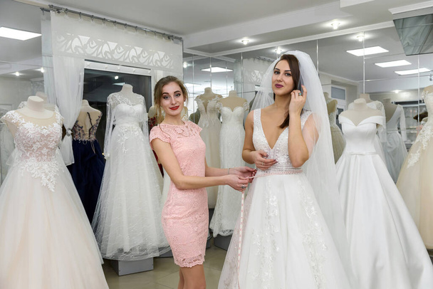 Verkäuferin im Hochzeitssalon hilft junger Braut - Foto, Bild