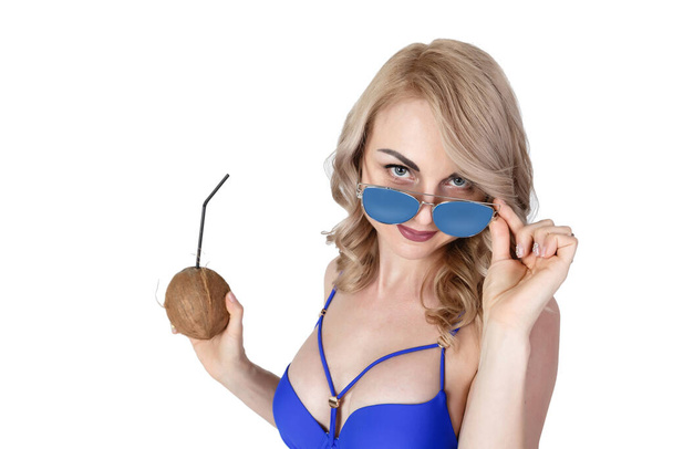 Nuori kaunis blondi nainen pukeutunut sinisiin uimapukuihin ja sinisiin aurinkolaseihin juoden mehua kookospähkinästä, katsoen kameraa. Eristetty valkoisella taustalla. Matkustuskäsite
 - Valokuva, kuva