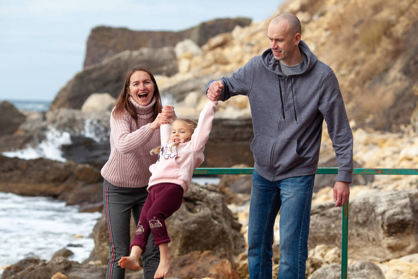Happy familie wandelingen op een houten pier blootsvoets tegen de achtergrond van de zee en rotsen, lente, buiten - Foto, afbeelding
