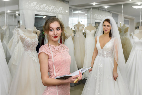 Dressmaker with notepad in wedding salon and bride - 写真・画像