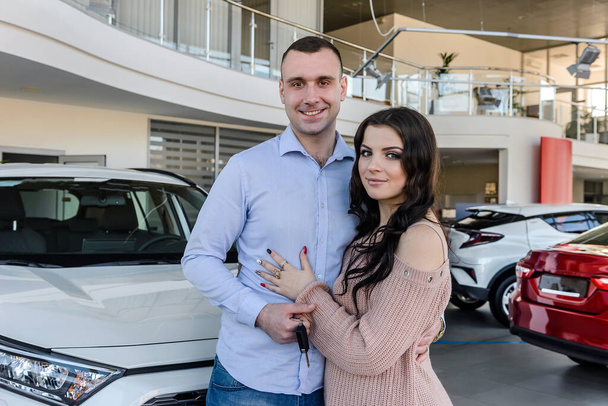 Happy couple posing with new cars in showroom - Photo, Image