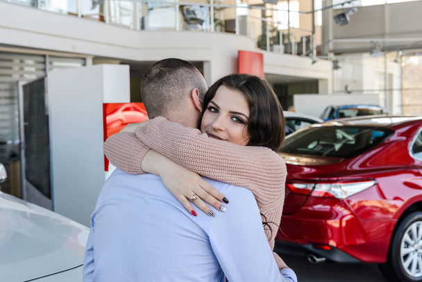 Happy couple posing with new cars in showroom - Fotoğraf, Görsel