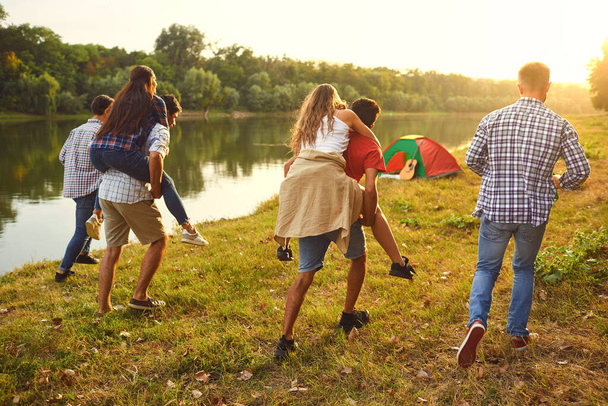 Friends have fun running along the lake on a picnic. - 写真・画像