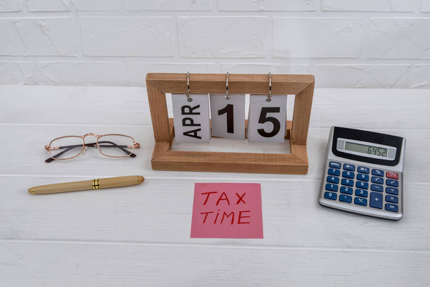 Податковий час з дерев'яним календарем, калькулятором, окулярами і ручкою
 - Фото, зображення