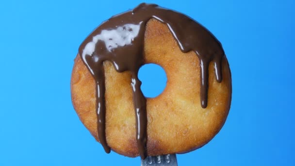 Grote ronde donut op een vork waarop chocolade glazuur en blauw poeder draaien op een blauwe achtergrond - Video