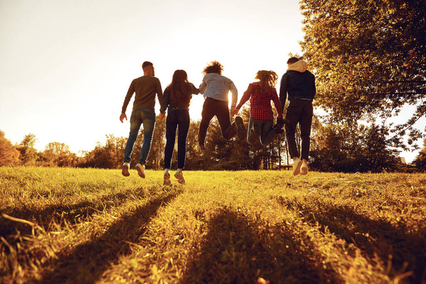 A group of young people jumping on the grass in the park at sunset. - Foto, Imagen