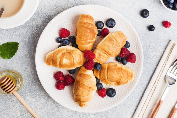 Croissants with fresh raspberries and blueberries on a dark concrete background. Copy space. concept of Breakfast coffee honey - Foto, Imagen