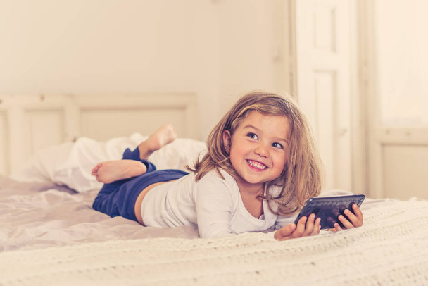 Little caucasian girl on mobile phone playing, watching cartoons or chatting with family. Cute blonde toddler using smart phone In Education and technology, digital generation and phone addiction. - Photo, image