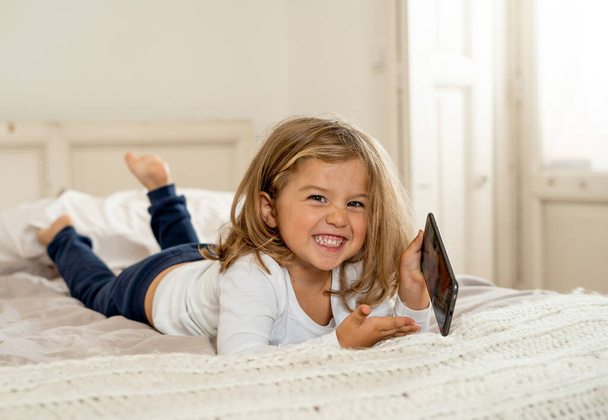 Little caucasian girl on mobile phone playing, watching cartoons or chatting with family. Cute blonde toddler using smart phone In Education and technology, digital generation and phone addiction. - Foto, Imagen