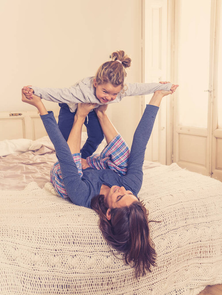 Happy family. Mother and cute daughter hugging, playing and laughing together in bed at home. Beautiful little girl having fun with mom in bonding time, single parent and education concept. - 写真・画像