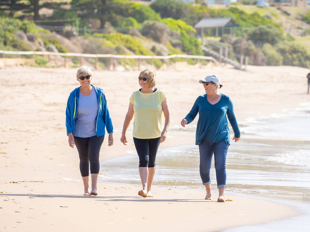 Lovely group of three active senior woman on their 60s walking, exercising and having fun on the beach. Mature females Laughing enjoying walk on vacation. Retirement and health lifestyle. - Photo, Image