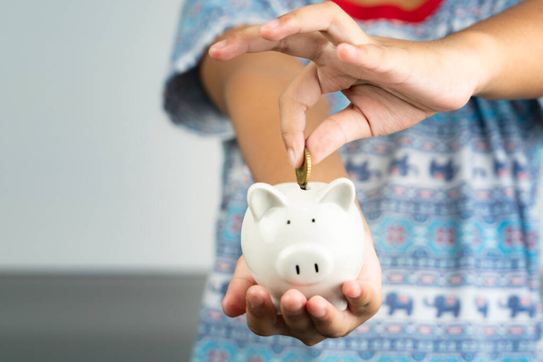 Spar- und Spendenkonzept: Kind legt Geld auf süßes weißes Sparschwein - Foto, Bild
