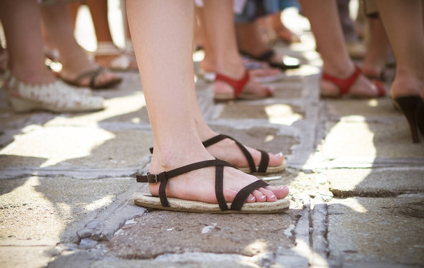Widok boczny upraw samicy w modnych czarnych sandałach stojących z innymi kobietami na brukowanej ulicy w słoneczny dzień - Zdjęcie, obraz