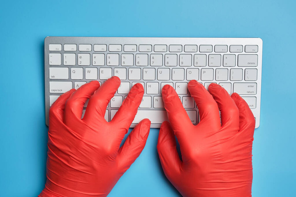 Kırmızı eldivenli doktor mavi arka planda bir klavyeye yazı yazıyor. Üst görünüm. - Fotoğraf, Görsel