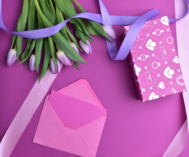Kukkakimppu violetti tulppaanit, violetti tausta, violetti ja vaaleanpunainen nauhat, vaaleanpunainen kirjekuori ja lahjapaketti, Top view
 - Valokuva, kuva