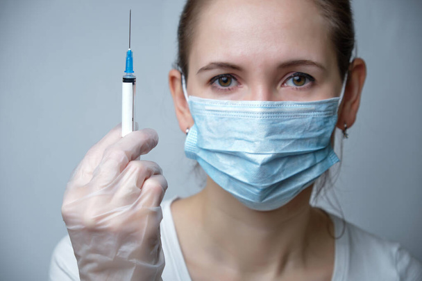 A nurse in a protective mask and gloves holds a syringe with copy space. Close up. - Photo, image