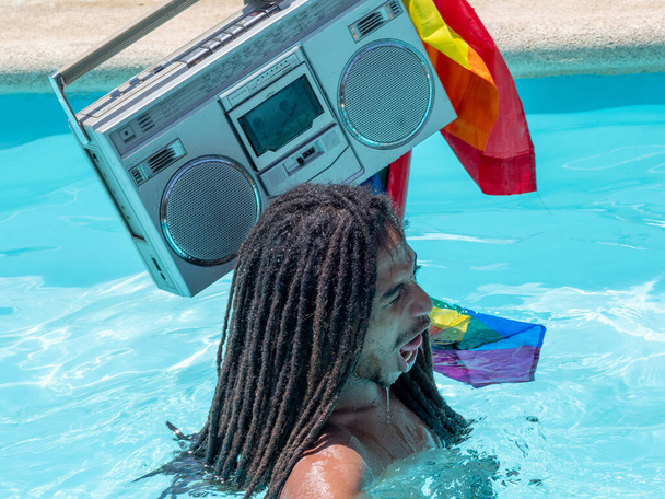 Photo d'un garçon noir avec des dreadlocks dans la piscine avec une cassette sur son épaule et souriant et avec une expression de respiration profonde. Mode de vie
 - Photo, image