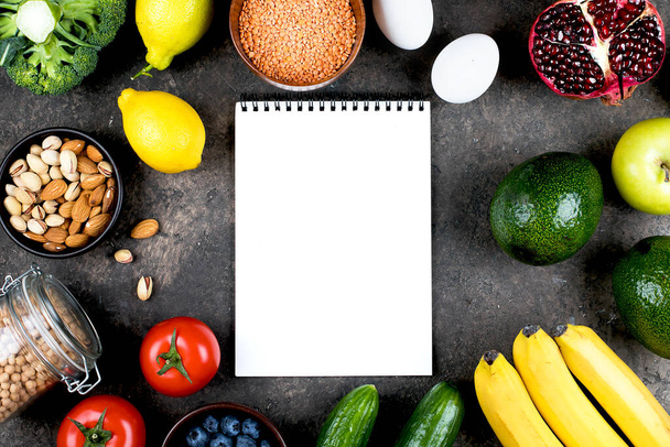 フードモックアップレシピのコンセプト。緑の野菜、トマト、ナッツ、果物、レンズ豆、ひよこ豆、緑、灰色のコンクリートテーブルの上に空白のノートブック。フラットレイアウト、トップビュー、コピースペース - 写真・画像