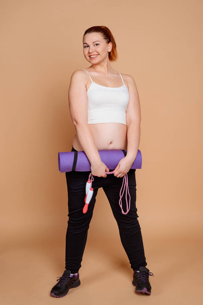 Positive woman holding fitness equipment: a mat and a jump rope - Foto, afbeelding