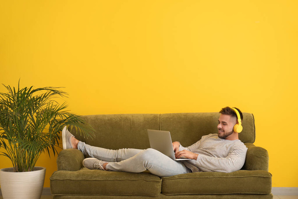 Young man with laptop and headphones resting on sofa at home - Φωτογραφία, εικόνα