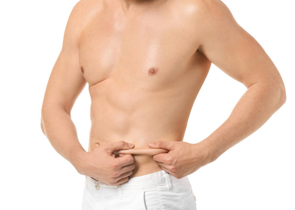 Przystojny młodzieniec dotykający tłuszczu na brzuchu na białym tle. Koncepcja chirurgii plastycznej - Zdjęcie, obraz