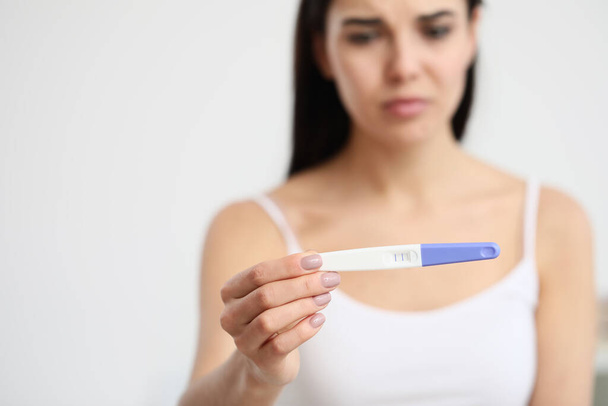 Sad young woman with pregnancy test in bathroom, closeup - Photo, Image