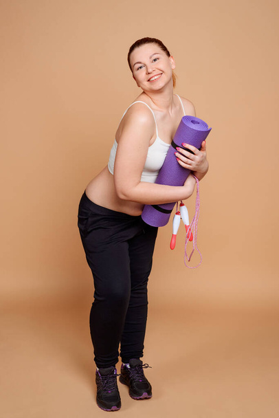Beautiful plus size woman holding a rolled mat and a jump rope - Foto, immagini