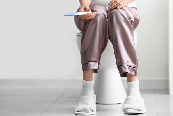 Jeune femme avec test de grossesse dans les toilettes
 - Photo, image