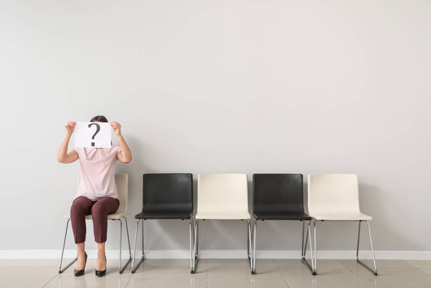 Young woman holding paper sheet with question mark while sitting on chair indoors. Job interview concept - Photo, Image