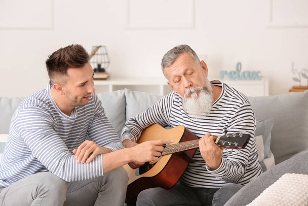 Молодий чоловік з батьком грає на гітарі вдома
 - Фото, зображення