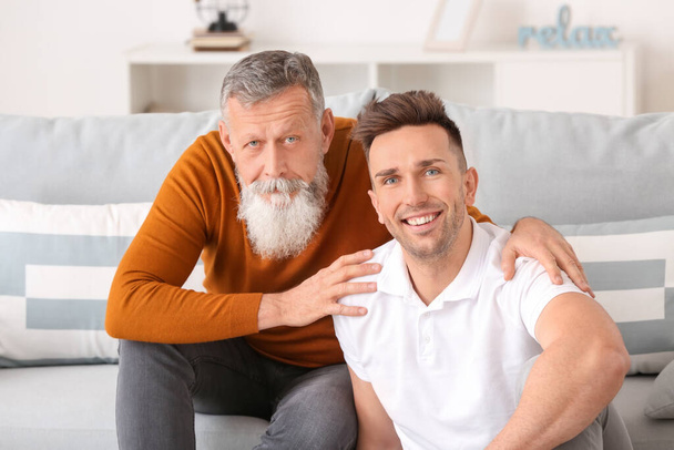 Portret van een oudere man en zijn volwassen zoon thuis - Foto, afbeelding