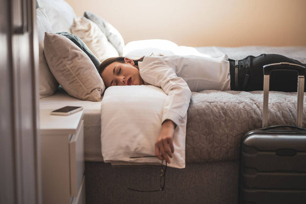 Η κουρασμένη επιχειρηματίας κοιμάται ντυμένη στο δωμάτιο του ξενοδοχείου.. - Φωτογραφία, εικόνα