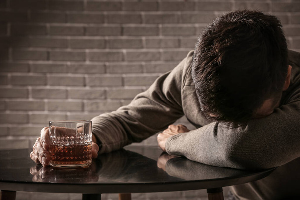 Депресивний молодий чоловік п'є алкоголь в приміщенні
 - Фото, зображення