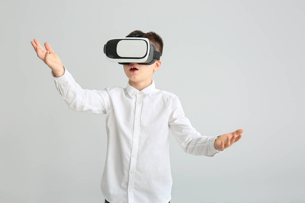 kleiner Junge mit Virtual-Reality-Brille auf grauem Hintergrund - Foto, Bild