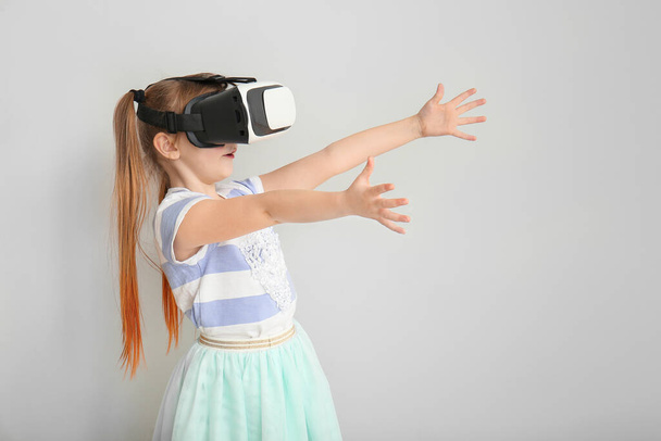 Işık arka planında sanal gerçeklik gözlüklü küçük kız - Fotoğraf, Görsel