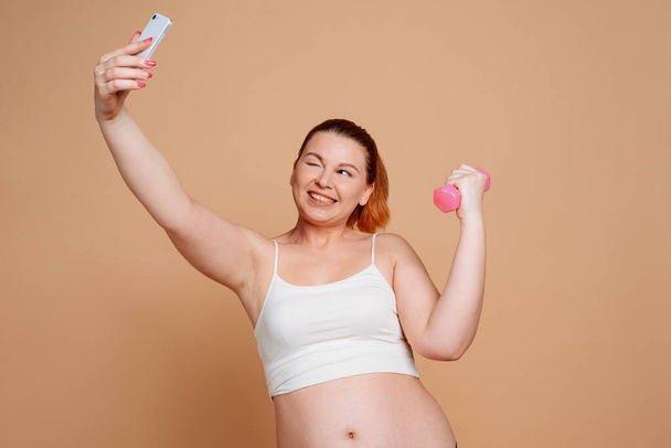 Woman taking a selfie during workout. Winking and posing with a dumbbell - Fotoğraf, Görsel