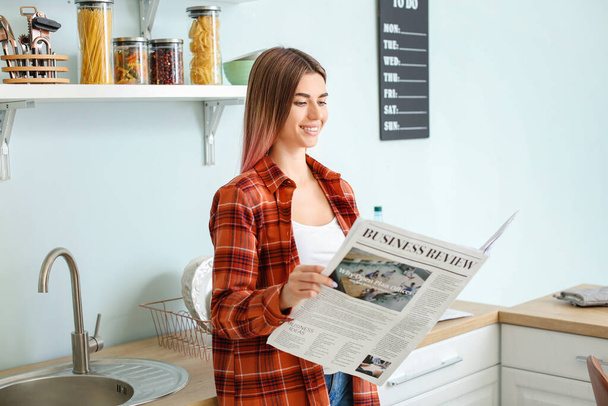 Beautiful young woman reading newspaper in kitchen - Photo, Image