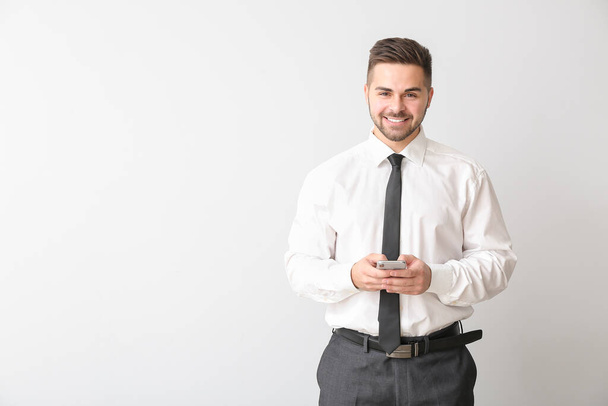 Young businessman with mobile phone on light background - Fotografie, Obrázek