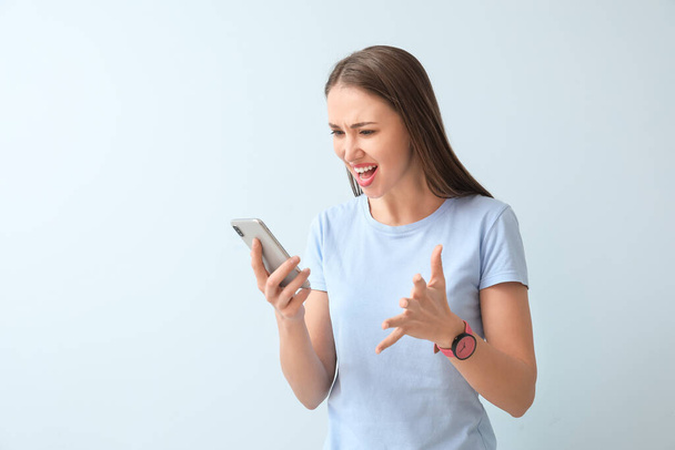 Angry young woman with mobile phone on color background - Foto, afbeelding