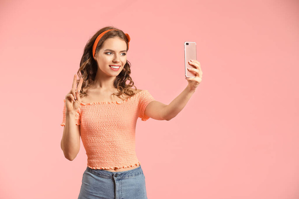 Young woman with mobile phone taking selfie on color background - Foto, Imagem