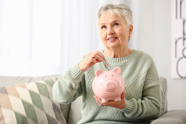 Vanhempi nainen laittaa rahaa säästöpossu kotona
 - Valokuva, kuva