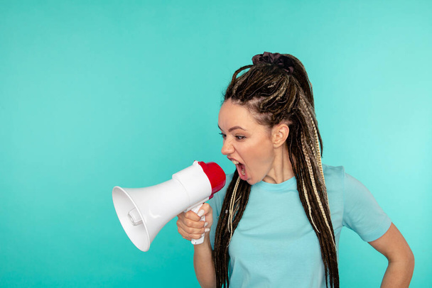 Angry woman screaming to the loudspeaker isolated over the blue background. - Foto, Imagem