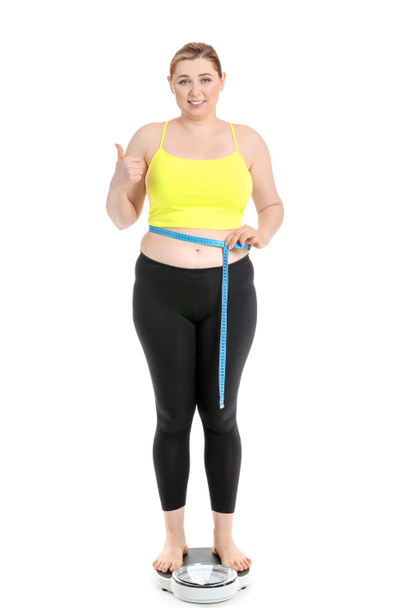 Mujer con sobrepeso de pie sobre escamas sobre fondo blanco. Concepto de pérdida de peso
 - Foto, Imagen
